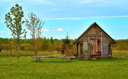 One old wooden hut on the green lawn and amid a blue sky with horizonの写真素材