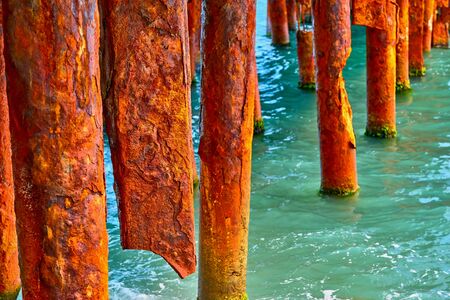 old red abstract rusty and ruined piles or props from pipes stick out in green water closeup with selective sharpnessの写真素材