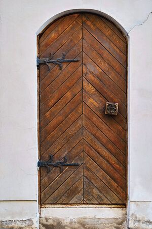 Old wooden door with forged canopies and hinges is located in a plastered stone wall closeupの写真素材