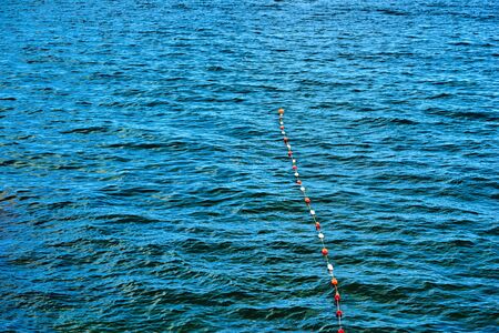 continuous seawater surface of blue with a small wave and small buoys in a row for fencing and safetyの写真素材
