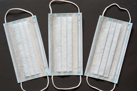 three individual disposable medical masks for antibacterial and antimicrobial respiratory protection are located close-up on a dark backgroundの写真素材