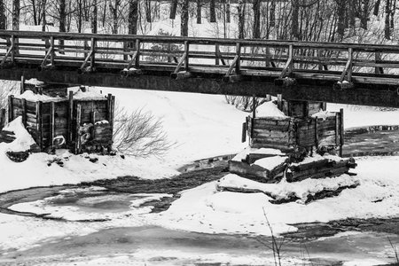 abstract empty old wooden bridge close-up on the river and with snow in winter or spring on a black and white photoの写真素材