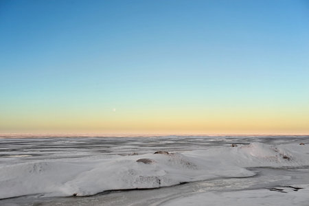 abstract northern spring landscape of the snowy surface of a large water space and with a yellow sunrise line on the blue sky horizonの写真素材