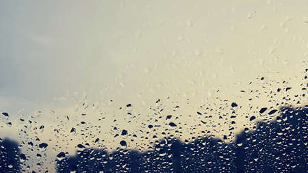 abstract background with raindrops on the glass of the window and with the silhouette of buildings against the background of an empty and clear skyの写真素材