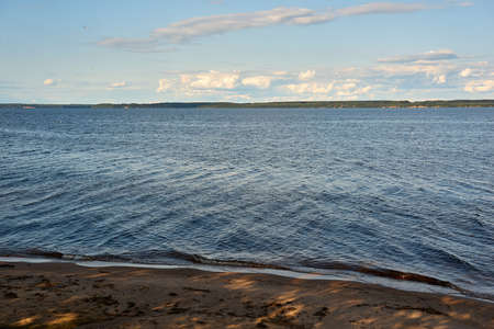 water landscape with part of the sandy shore in the foreground, with forest on the horizon and skyの写真素材