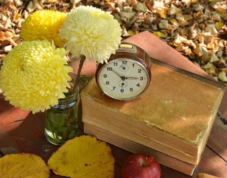 Apples and brown clock on books with beautiful flowersの写真素材