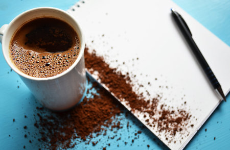 Cup of black coffee on blue background and blank paperの写真素材