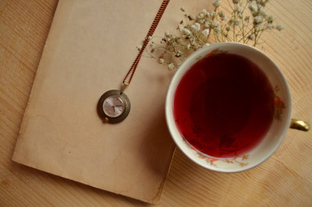 Tea cup, watch and old book on  wooden background