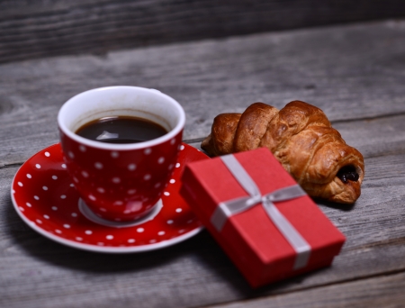 Cup of coffee with present and croissant on woodenの写真素材