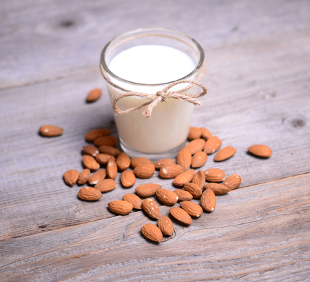 Almond milk in glass with almonds on wooden tableの写真素材