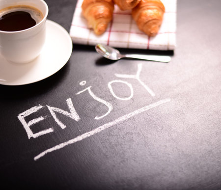 Croissant and cup of coffee with quote "ENJOY" on black backgroundの写真素材