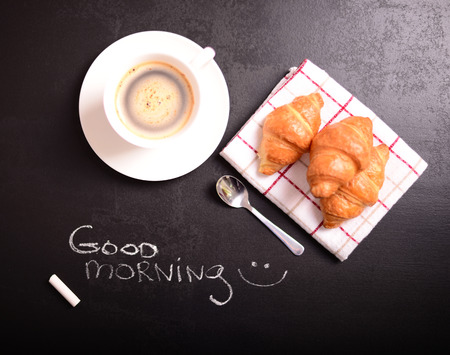 Croissant and cup of coffee with quote "GOOD MORNING" on black backgroundの写真素材