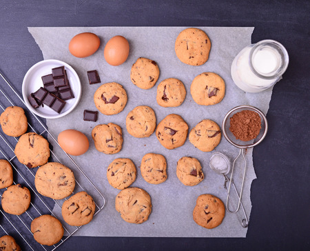 Home baked chocolate cookies on cooling rack and baking paper with ingredients on black backgroundの写真素材