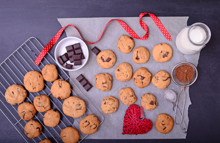 Home baked chocolate cookies on baking paper with ingredients on black background