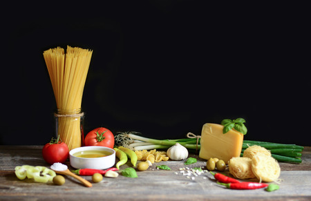 Italian and Mediterranean food ingredients on old wooden background. Spaghetti, olives, basil, cherry, tomato, pasta, garlic, pepper and oliveの写真素材