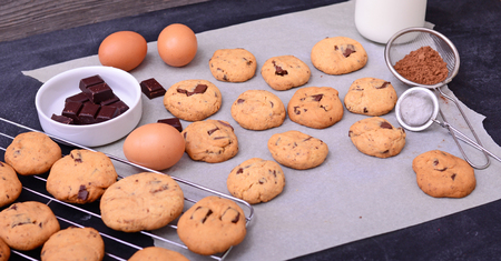 Home baked chocolate cookies  and ingredients on baking paper on black backgroundの写真素材