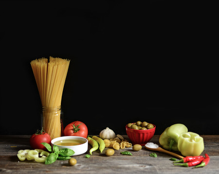 Italian and Mediterranean food ingredients on old wooden background. Spaghetti, olives, basil, cherry, tomato, pasta, garlic, pepper and oliveの写真素材
