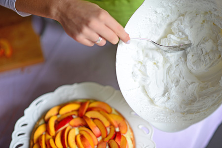 Woman hand put whipped cream on peach cakeの写真素材
