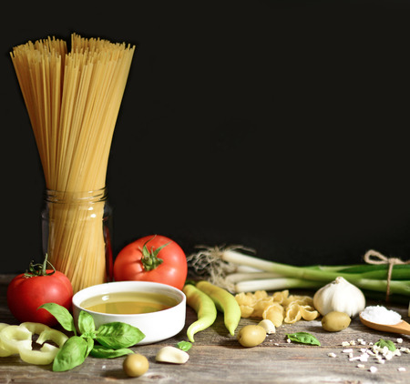 Italian and Mediterranean food ingredients on old wooden background. Spaghetti, olives, basil, cherry, tomato, pasta, garlic, pepper and oliveの写真素材