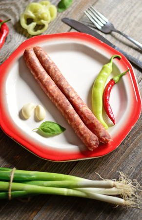 Portion of sausages on plate with tomatoe, fresh onion, chilly peppers and olives on wooden backgroundの写真素材