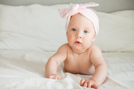 Little pretty girl in a pink bandage on her head lies on a bed on a white sheet