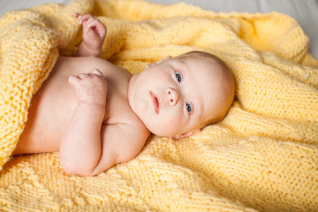 Cute infant baby looking at camera in a knitted yellow plaid on a white bed. Copyspace