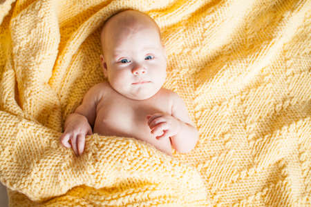 Cute infant baby looking at camera in a knitted yellow plaid on a white bed. Copyspaceの写真素材