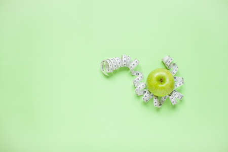 Diet and healthy eating concept. Top view of weightloss. Green apple and measuring tape. Green backgroundの写真素材