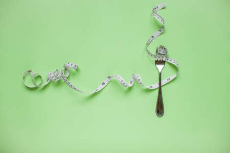 Diet and healthy eating concept. Top view of weightloss. Measuring tape on a fork. Green backgroundの写真素材