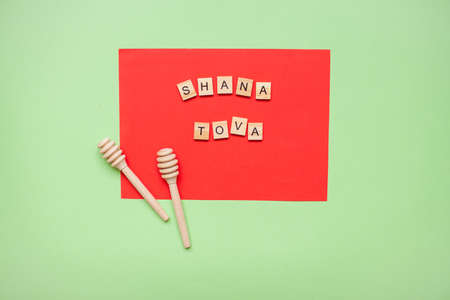 Words from wooden blocks "shana tova" and wooden spoons for honey on a red and green background. Rosh hashanahの写真素材