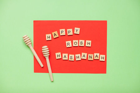 Words from wooden blocks happy rosh hashanah and wooden spoons for honey on a red and green...