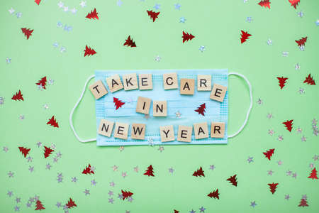 inscription from wooden blocks take care in new year on a medical protective mask and on a new year backgroundの写真素材