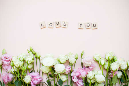 Inscription of wooden blocks love you. Delicate touching bouquet of white and pink flowers on a light pink background. Layout. Flat layの写真素材