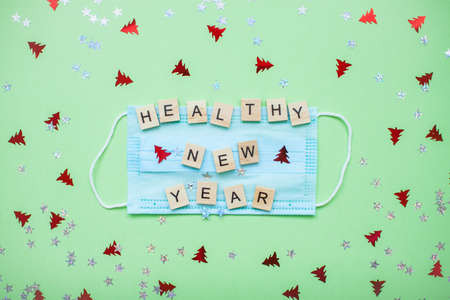 inscription from wooden blocks of a healthy new year on a medical protective mask and on a new year backgroundの写真素材