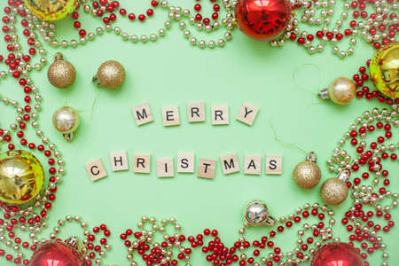 inscription merry christmas in a Christmas frame of gold and red balls and beads on a green backgroundの写真素材