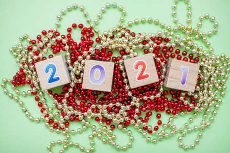 Happy New year 2021 celebration. The inscription 2021 from children's educational wooden cubes on a green background and New Year's decorations: gold and red shiny beadsの写真素材