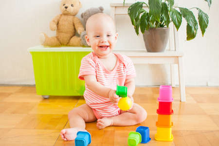 Little baby girl sitting on the floor, crawling and playing with brightly colored educational toys, pyramidsの写真素材