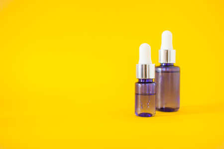 Cosmetic bottles with serum on a bright yellow background. Cosmetology and beauty concept.の写真素材