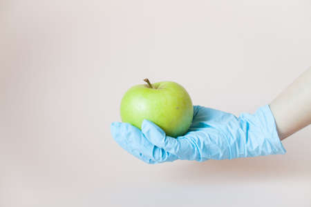 Green apple in hands in protective medical rubber gloves on a light background.の写真素材