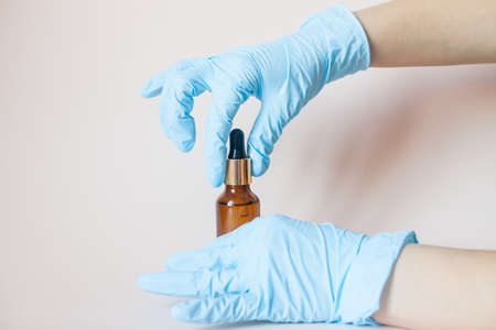 Bottles with serum for the face in his hands in protective medical rubber gloves on a light background. Beauty industry.の写真素材