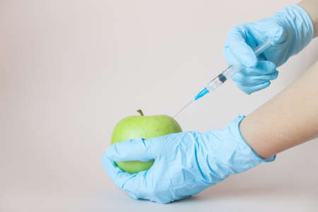 Green apple in hands with a syringe in protective medical rubber gloves on a light background.の写真素材