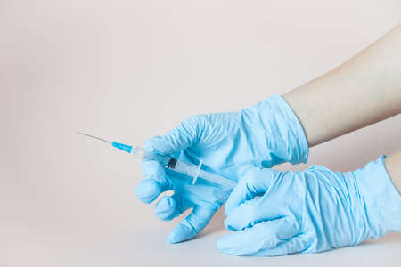 Syringe in hands in protective medical rubber gloves on a light background.の写真素材