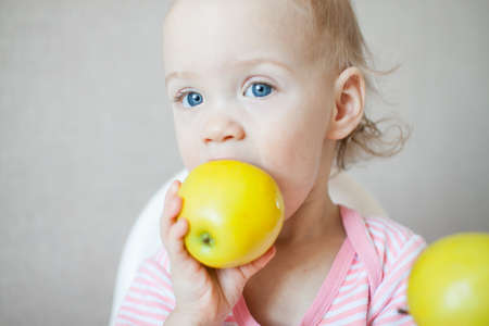 A little girl tastes, examines and plays with fresh apples with pleasure and interest. High quality photoの写真素材
