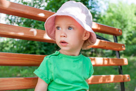Little girl in a green T-shirt and a pink panama walks in the park in the summer. High quality photoの写真素材