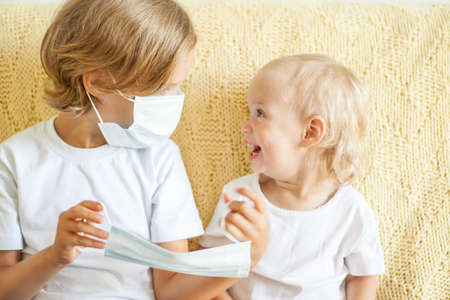 Portrait of two sisters putting on medical protective masks. The older sister helps the younger. Sisters playing fun. protection concept, quarantine. High quality photoの写真素材
