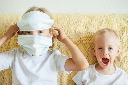 Portrait of two sisters putting on medical protective masks. The older sister helps the younger. Sisters playing fun. protection concept, quarantine. High quality photoの写真素材