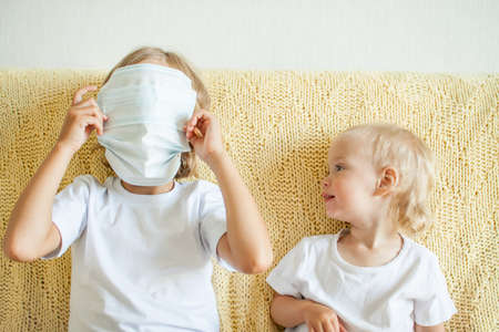 Portrait of two sisters putting on medical protective masks. The older sister helps the younger. Sisters playing fun. protection concept, quarantine. High quality photoの写真素材