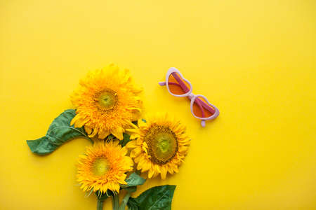 Arrangement of pink sunglasses in the shape of hearts and sunflowers on a bright yellow background. High quality photoの写真素材