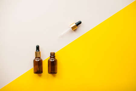 Cosmetic bottles for serum, oil or cream on bright yellow and light pink background. High quality photoの写真素材