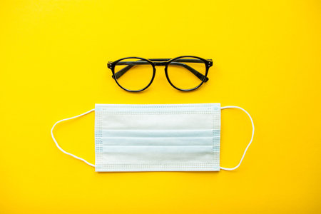 Flat lay. Medical protective mask and goggles on bright yellow background. High quality photo